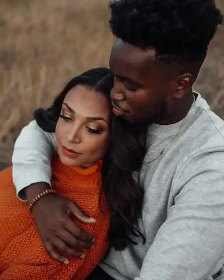 Couple embracing in tall autumn grass, she in a rust sweater