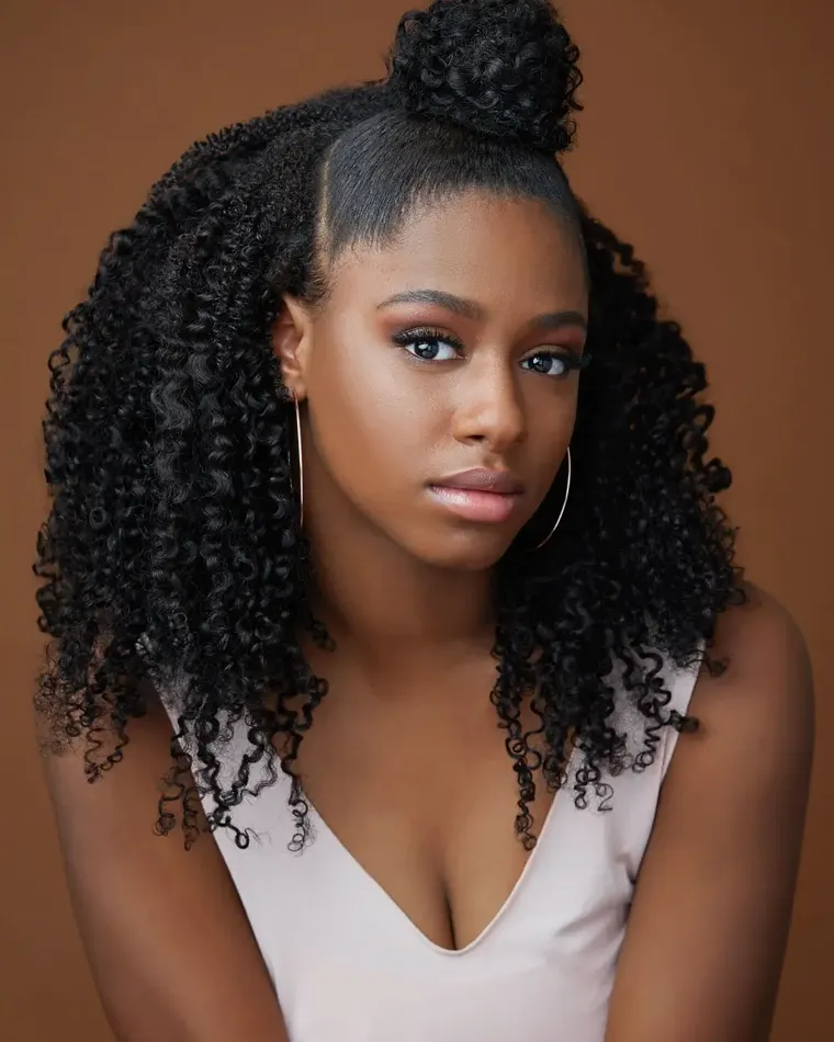 Headshot of a woman with curly hair in a top knot against a brown backdrop